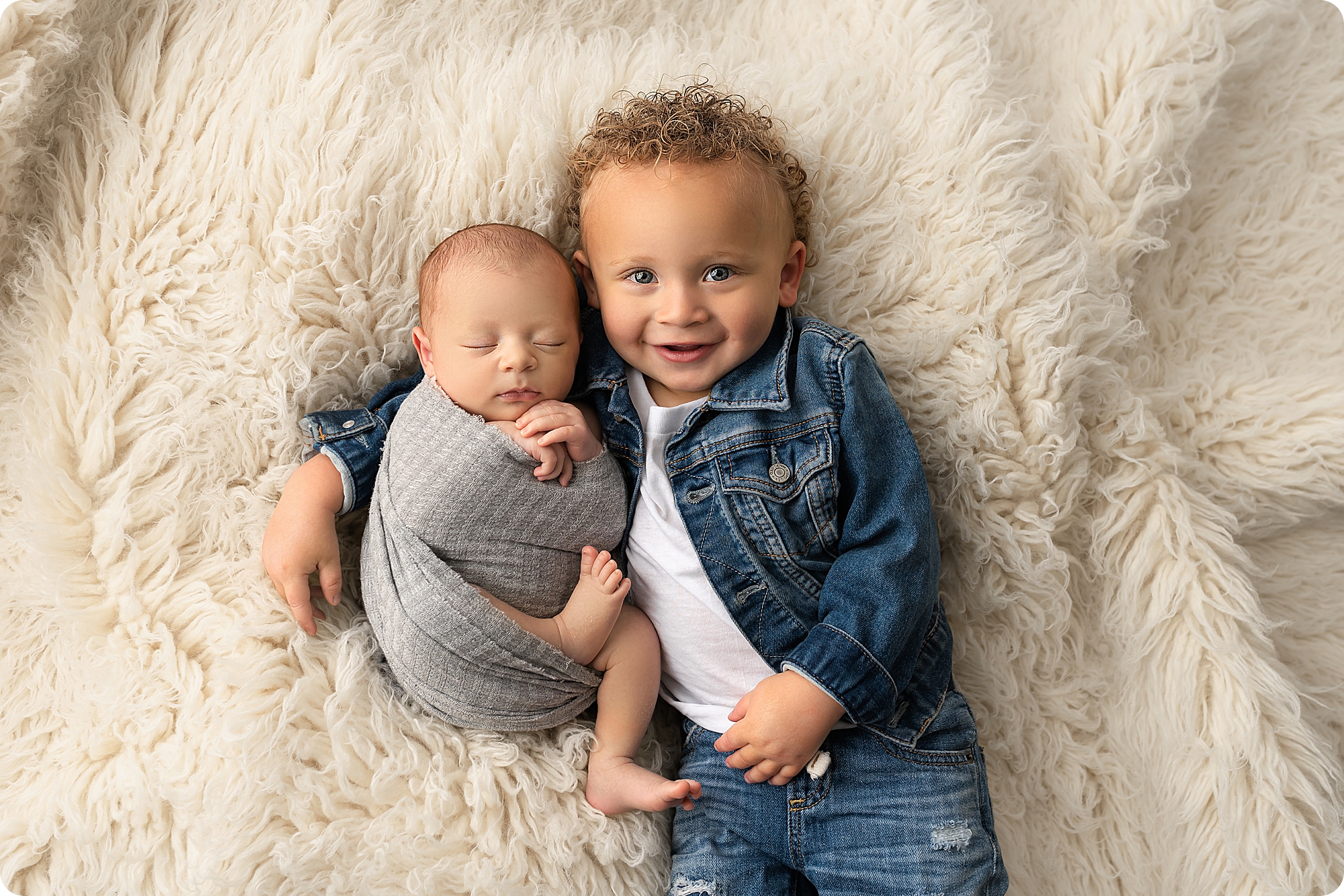 toddler holds baby brother in grey wrap during Utah newborn photos