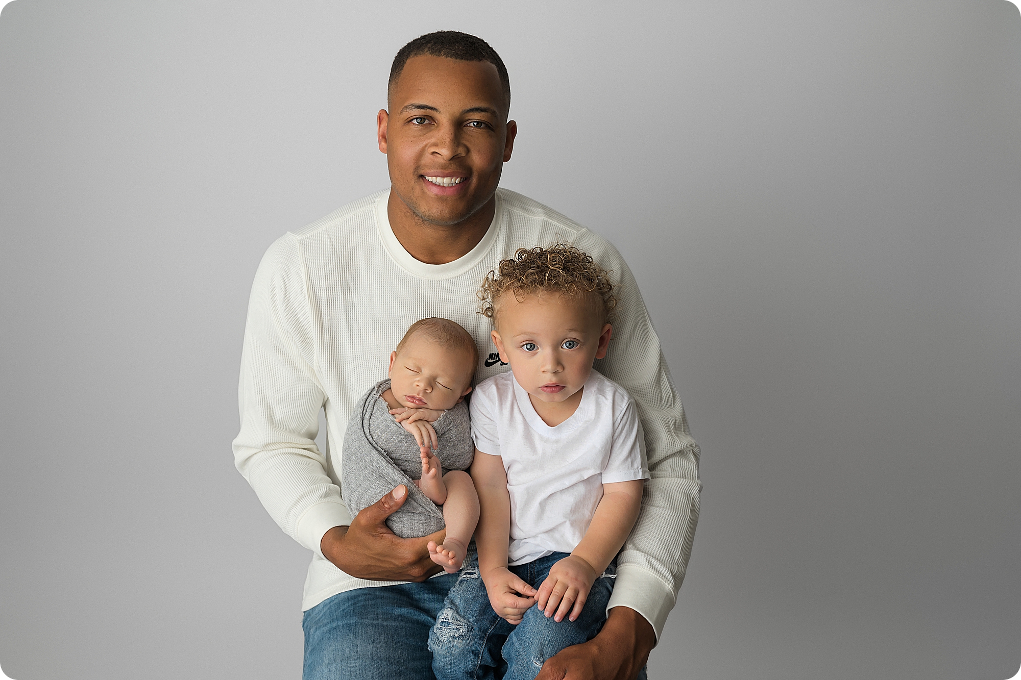 dad holds two sons in lap during Utah newborn session in studio