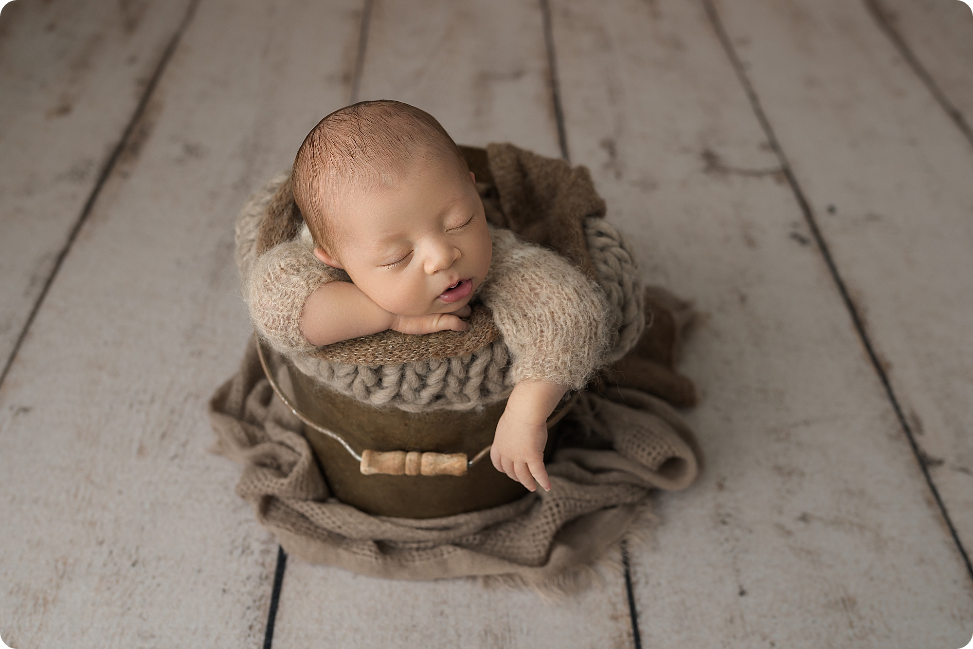 baby sleeps in brown bucket during newborn photos in studio
