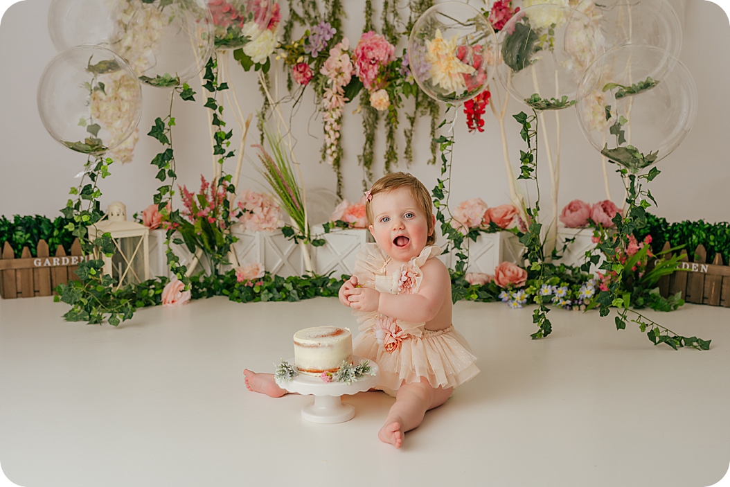 baby girl laughs during enchanted forest cake smash with naked cake in front of her