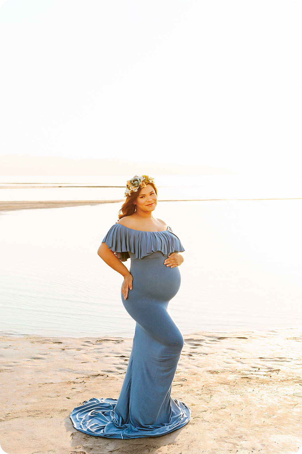 woman holds belly during maternity photos along beach in Utah