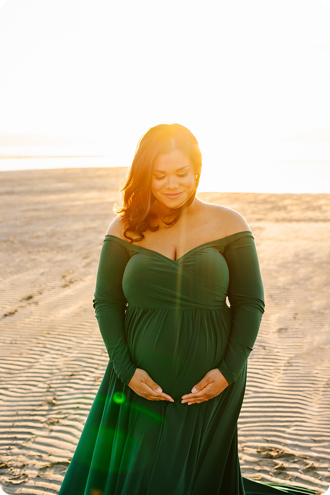 woman holds belly at sunset during waterfront maternity portraits 