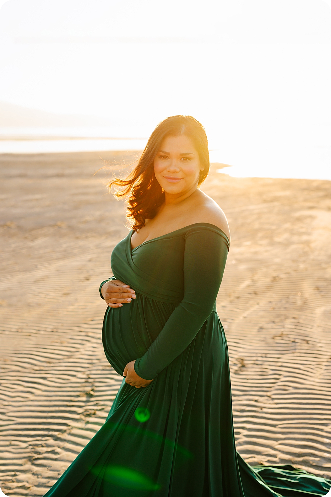 mother in emerald green maternity gown holds belly standing on sand in Utah 