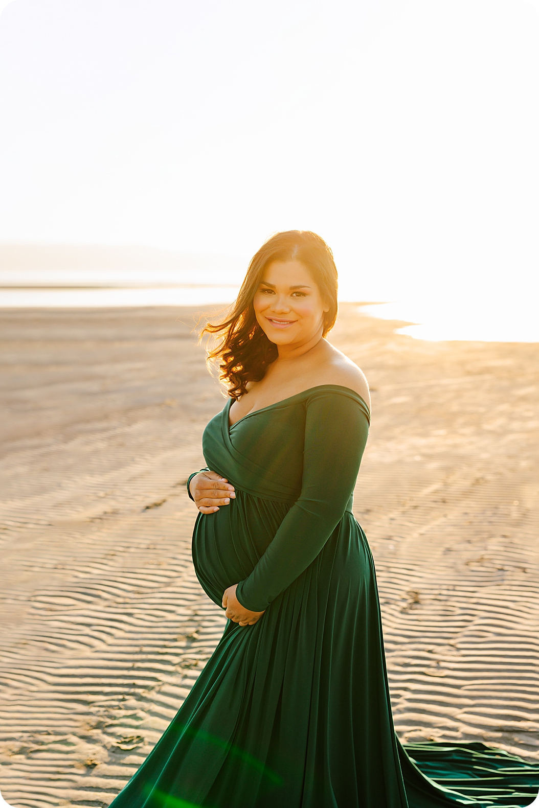 mother in emerald gown holds belly during waterfront maternity portraits 