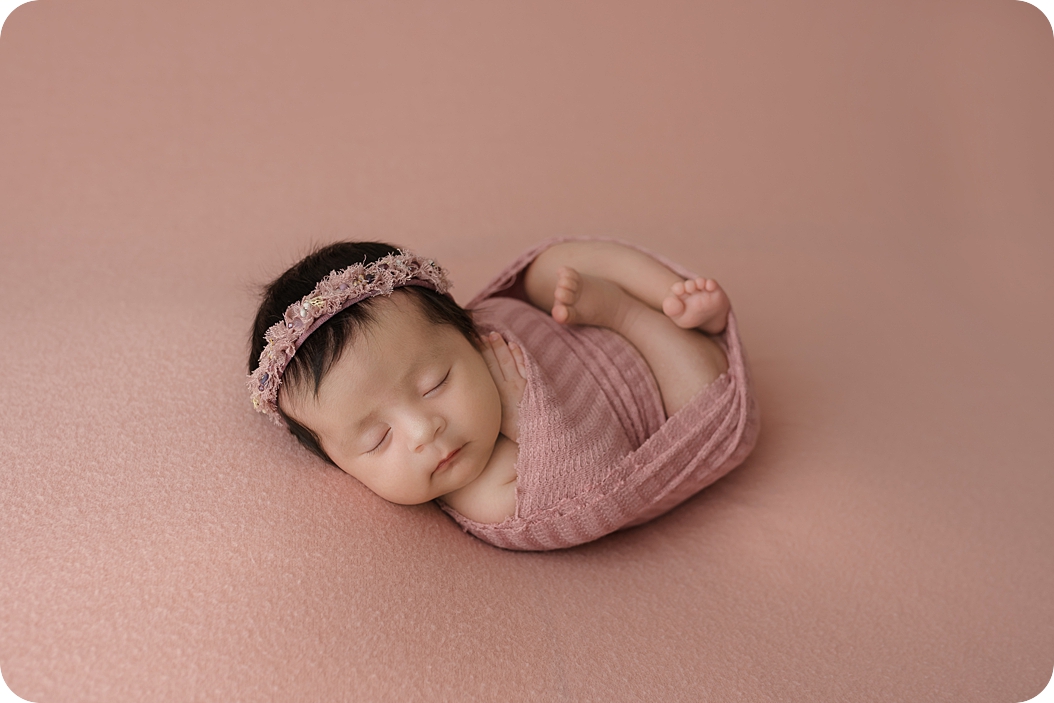 baby in pink wrap lays on pink backdrop during studio newborn portraits in Utah