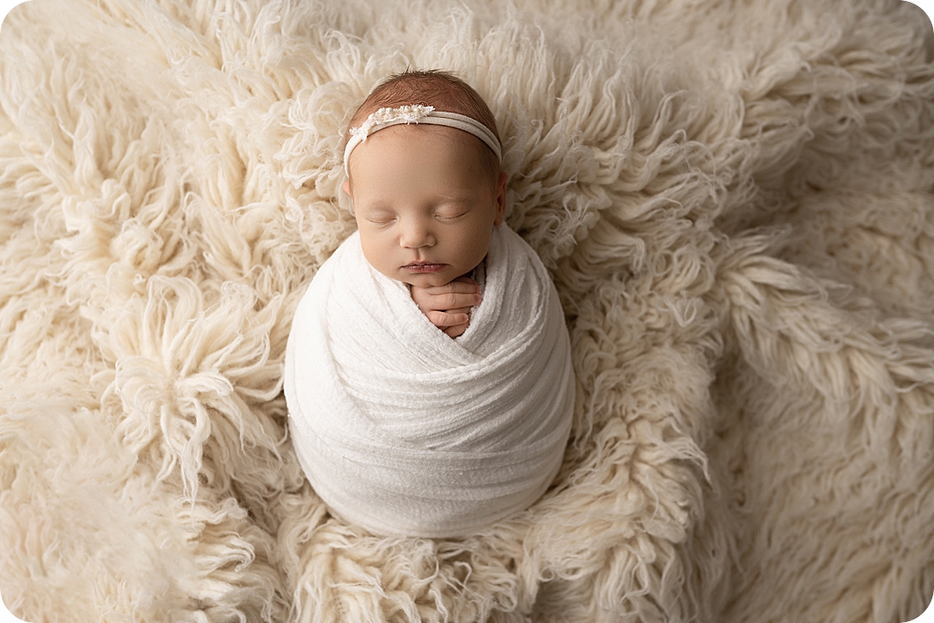 baby girl lays in white wrap during newborn photos in Utah studio