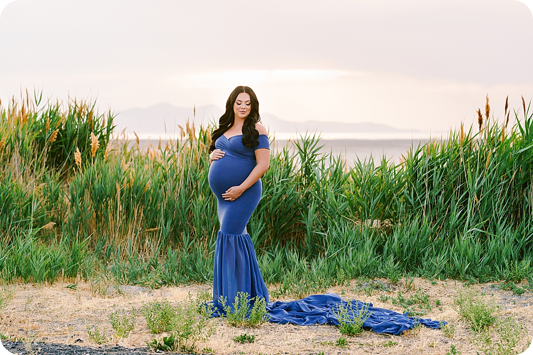 woman poses in tall grass wearing blue gown