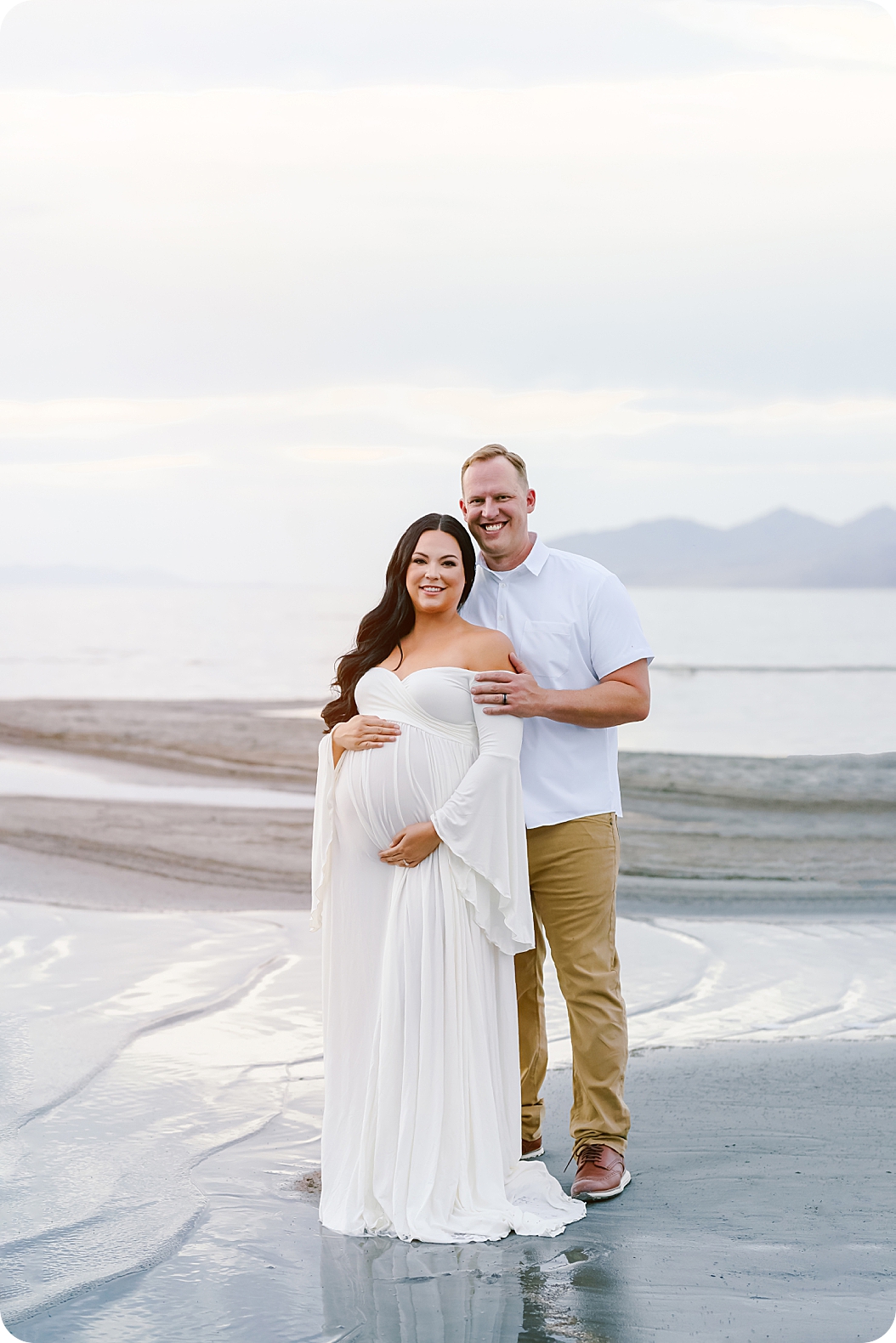 couple hugs by waterfront during Lakeside Maternity Portraits