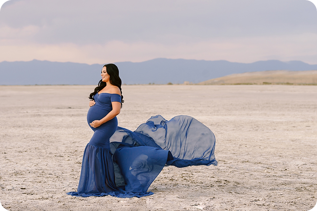 expectant mother in blue gown holds belly while skirt floats in air