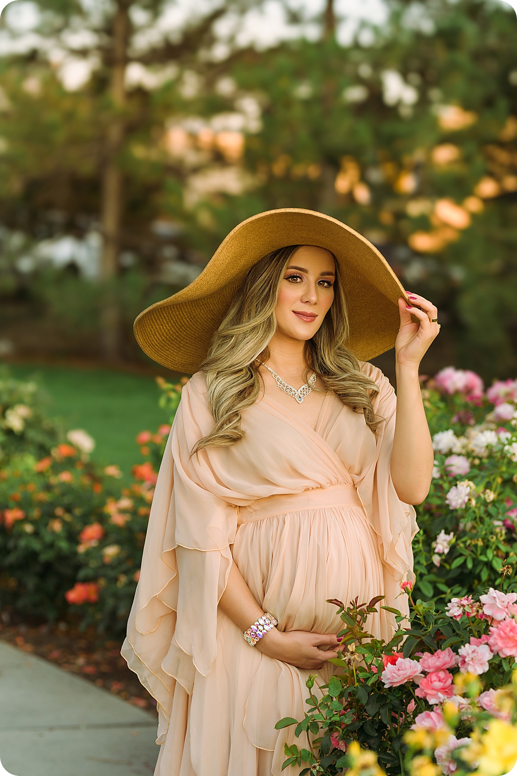 mom holds hat while standing in rose garden
