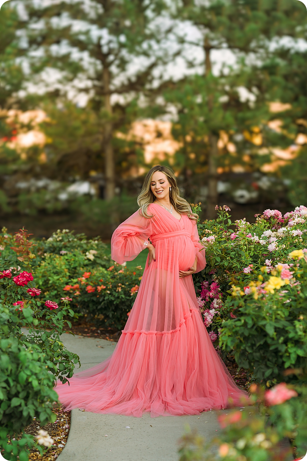 mom in pink gown holds belly during garden maternity session