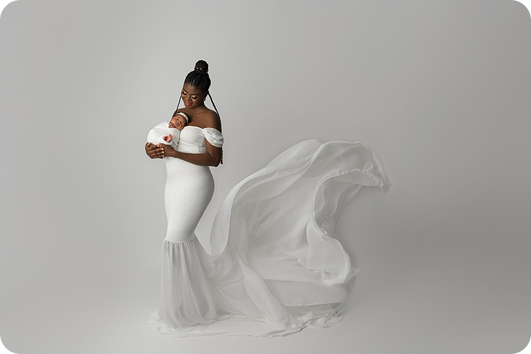 mom in white gown holds baby girl in white wrap