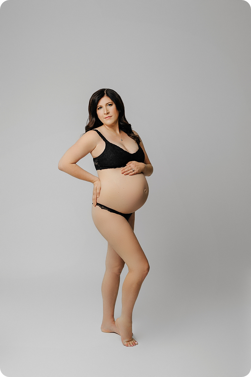 woman stands in black bra and panties for studio maternity session