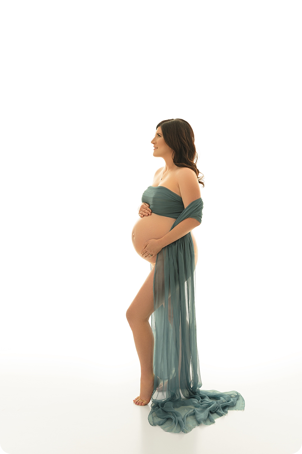 woman stands holding belly with green wrap during Utah studio maternity session