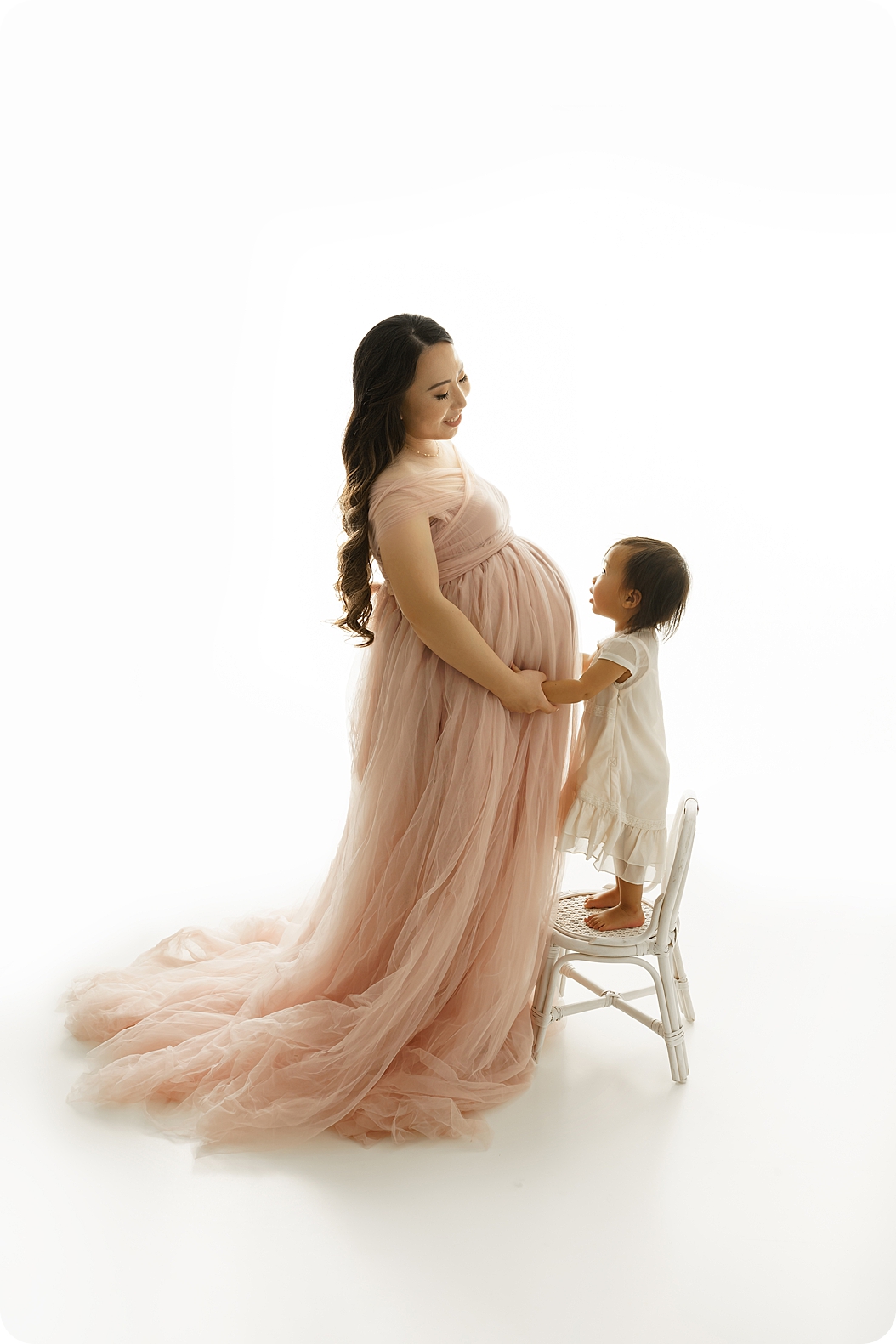 mom stand in studio with toddler on stool hugging belly during Timeless Studio Maternity Session