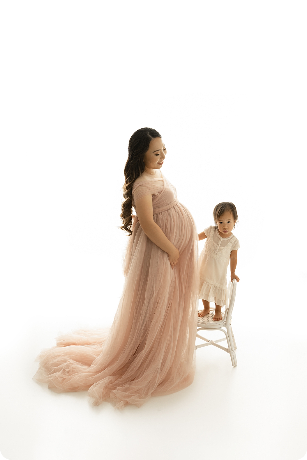 woman stands in studio with daughter during maternity photos