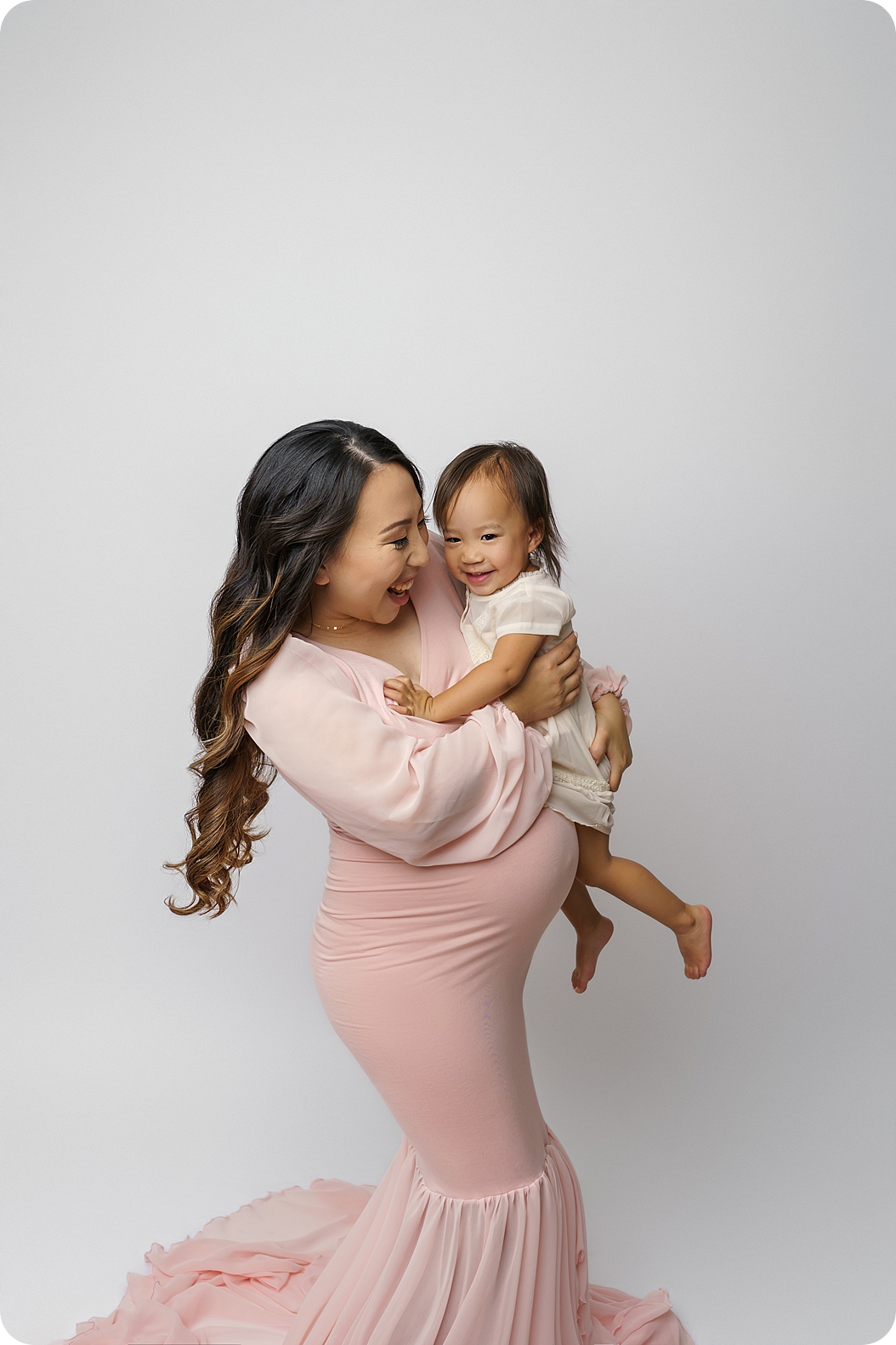 mom holds toddler daughter during maternity photos 