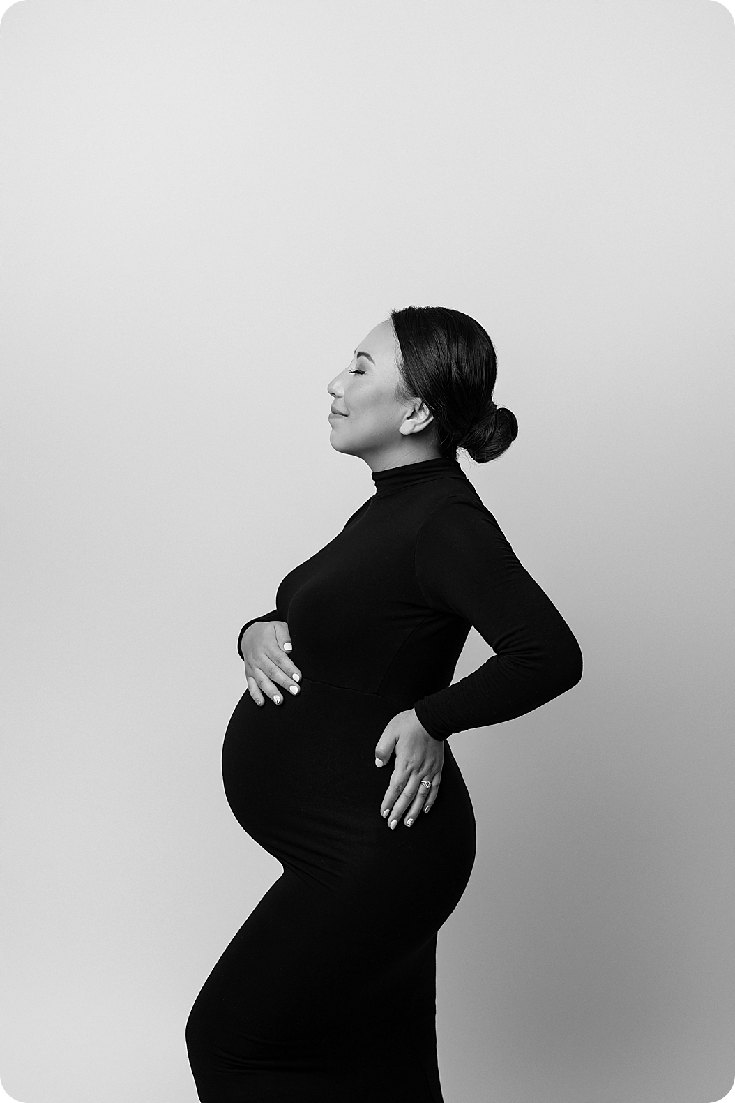 black and white portrait of mom with bun in black dress holding pregnant belly