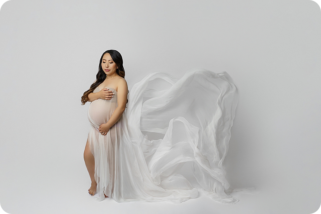woman in white dress holds belly during Timeless Studio Maternity Session