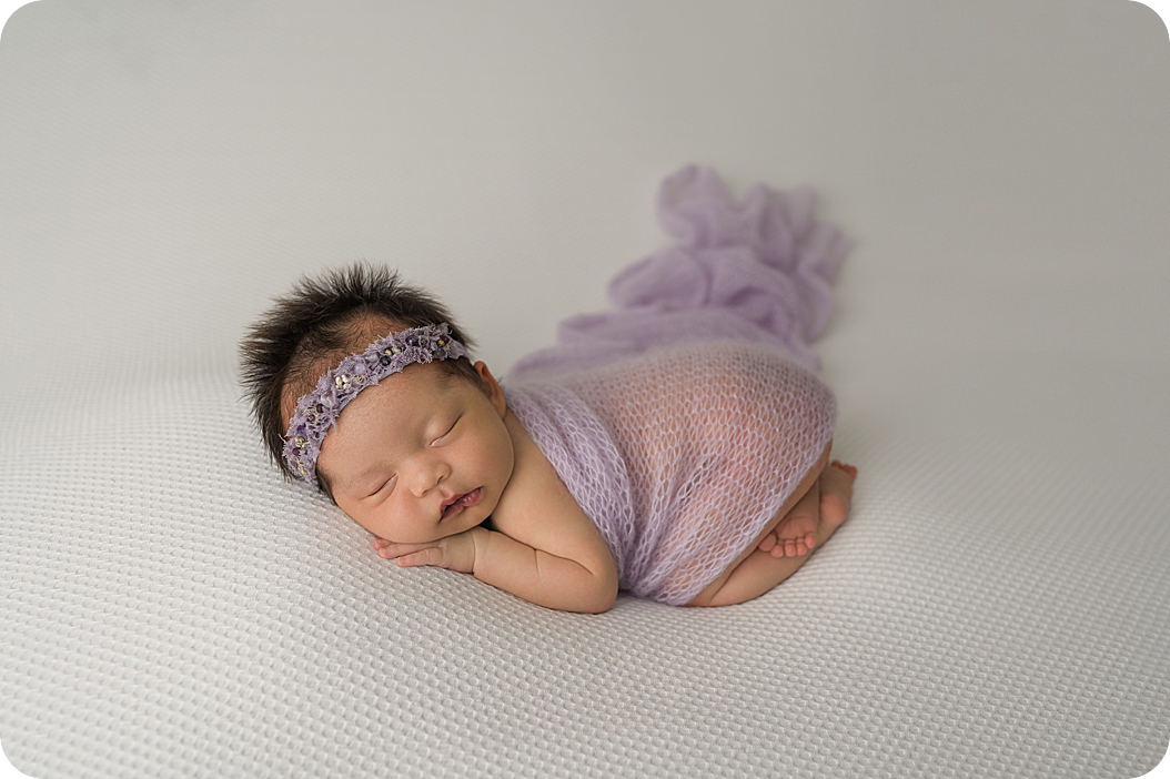 baby in purple wrap lays on white blanket