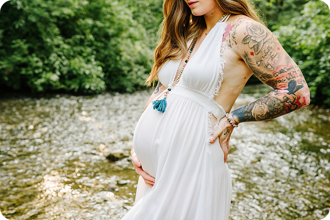 mom holds back and belly during canyon maternity portraits along the creek