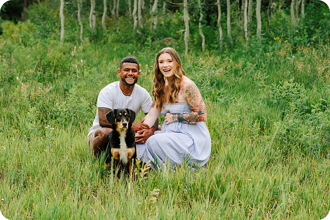 couple sits in field with dog during canyon maternity portraits in Utah