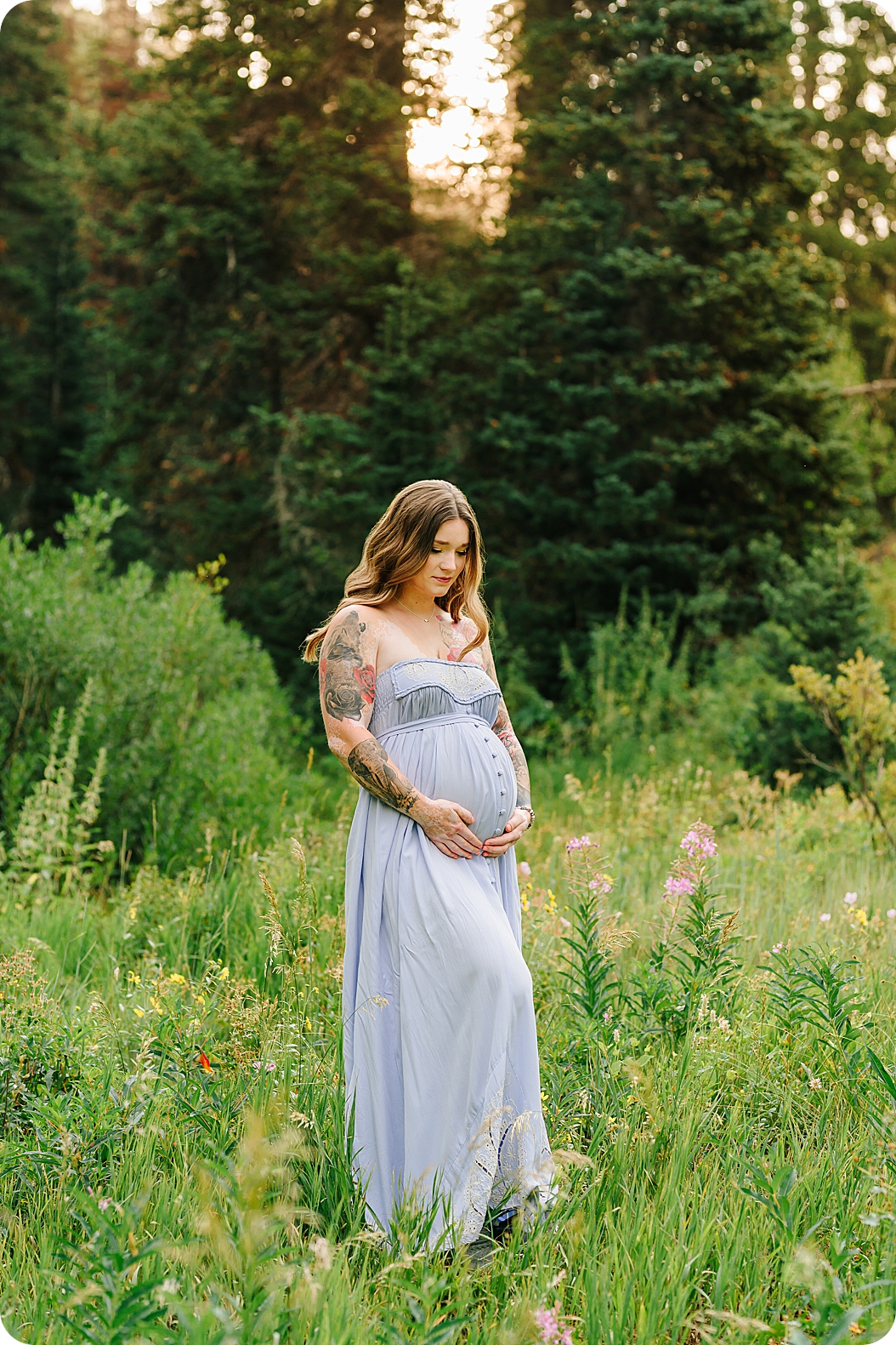 mother holds stomach in pale blue gown during canyon maternity portraits at sunrise