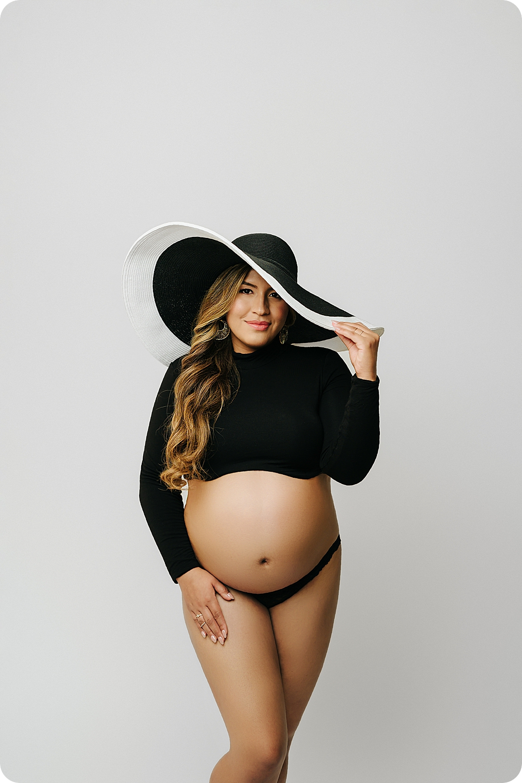 woman stands in black top with floppy hat during fashion inspired maternity session