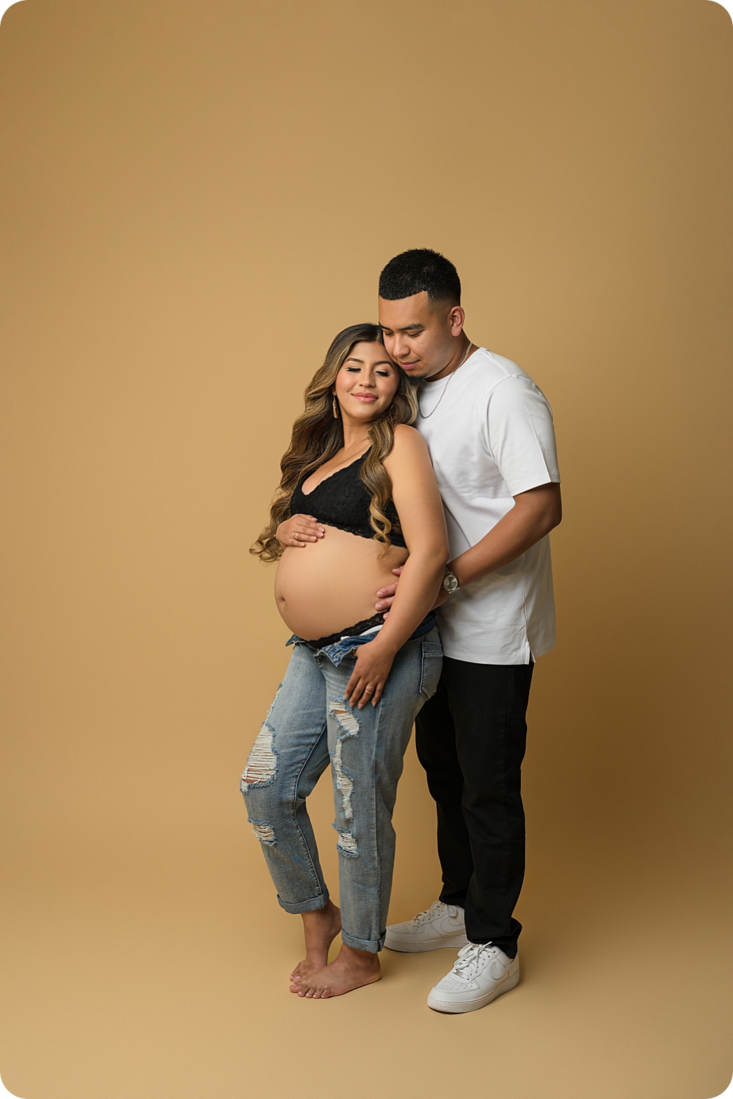 woman in black bra and jeans poses with partner during fashion inspired maternity session