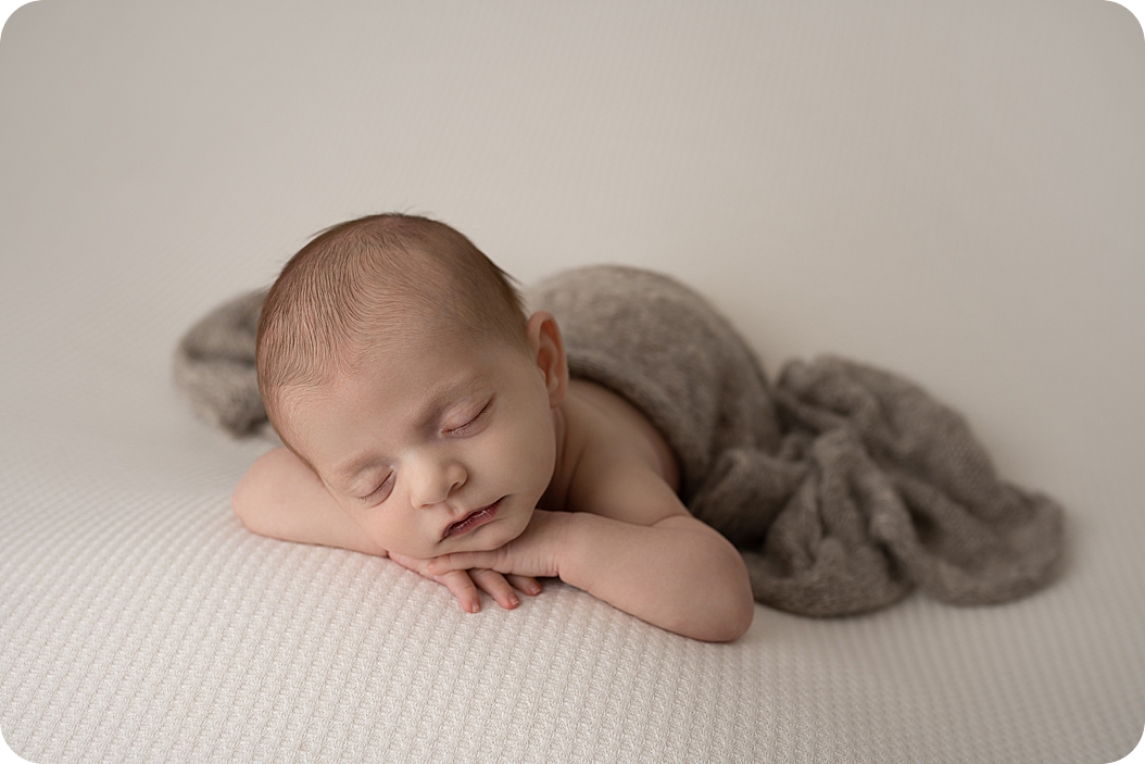 baby in brown blanket sleeps with hands under chin during neutral toned newborn session