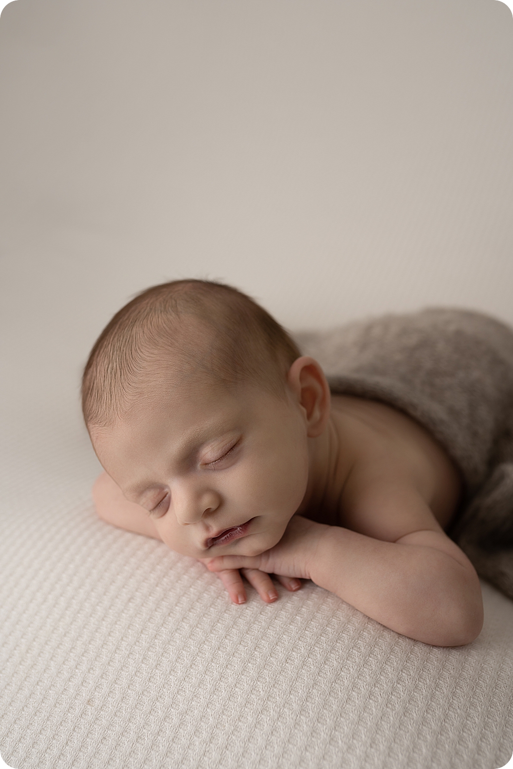 baby sleeps with hands under his chin during neutral toned newborn session