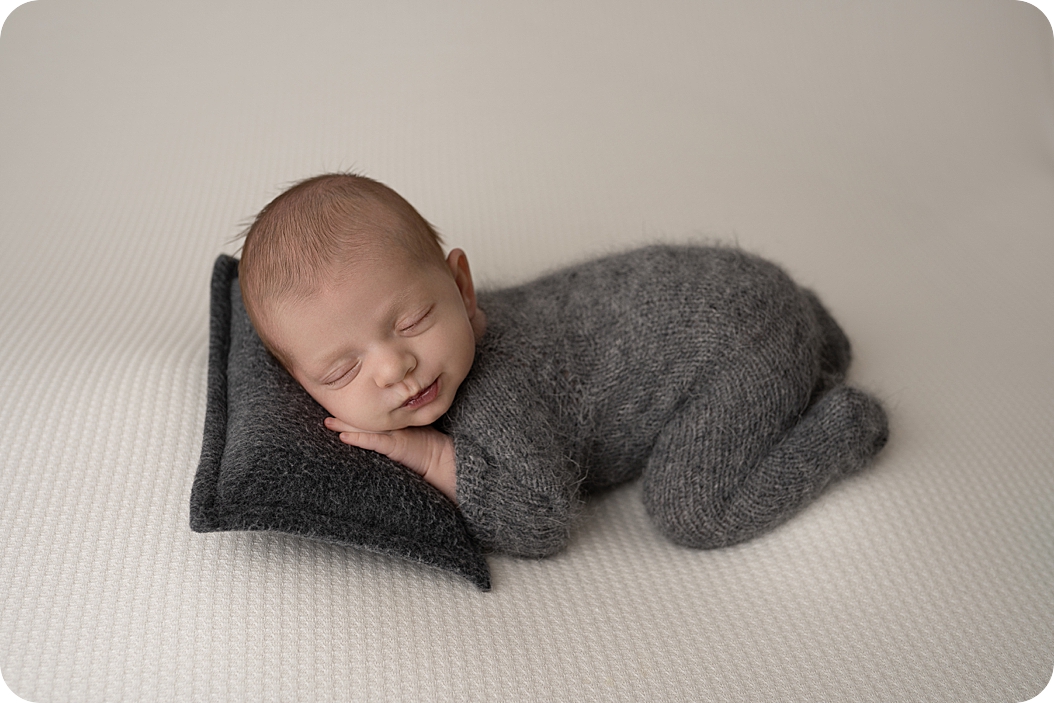 baby curls up in grey onesie during neutral toned newborn session