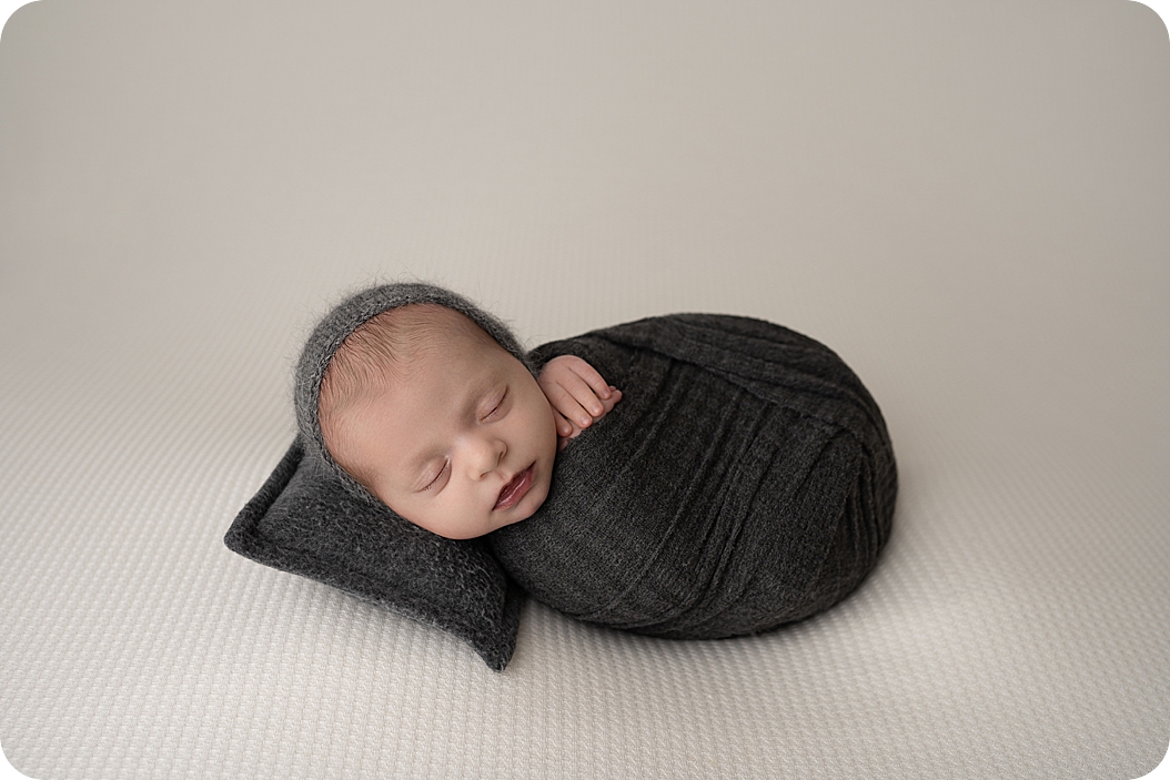 baby wrapped in dark blanket sleeps on fuzzy pillow