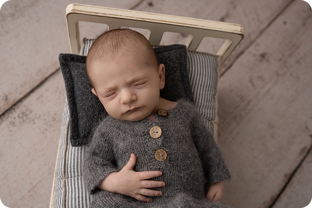 baby in grey button up outfit sleeps on tiny bed