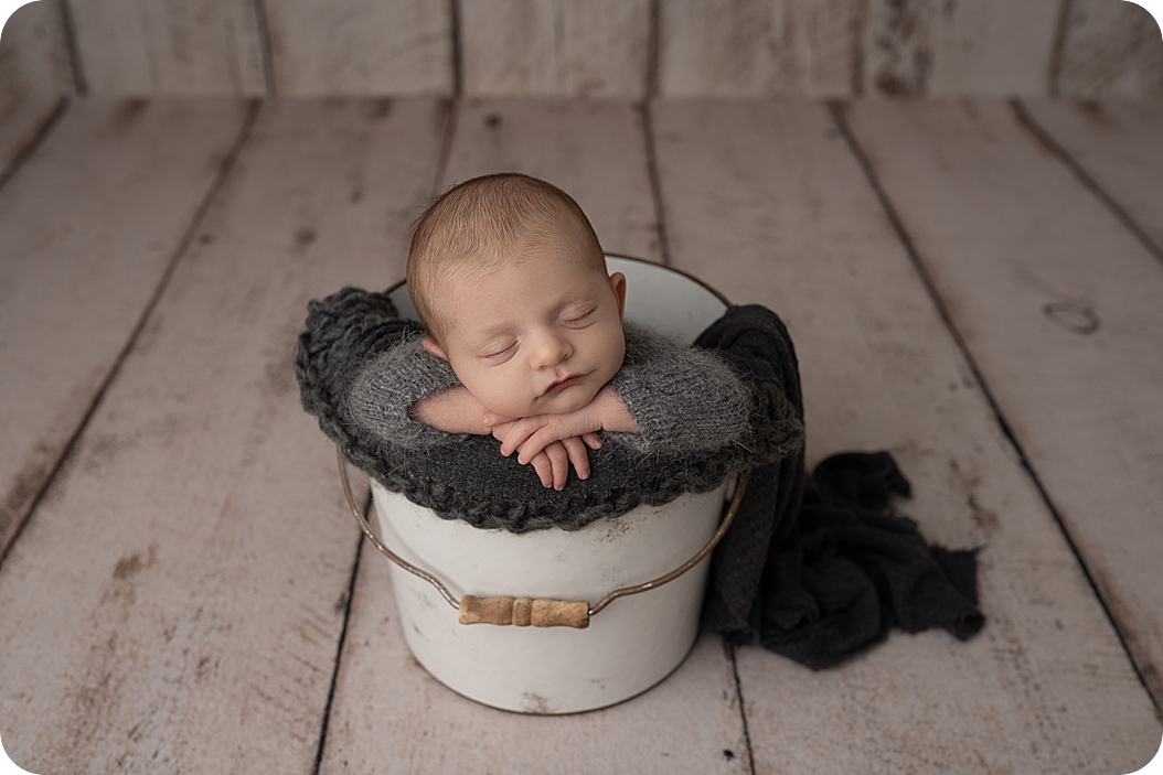 newborn baby sleeps in bucket on wooden floor in Utah studio 