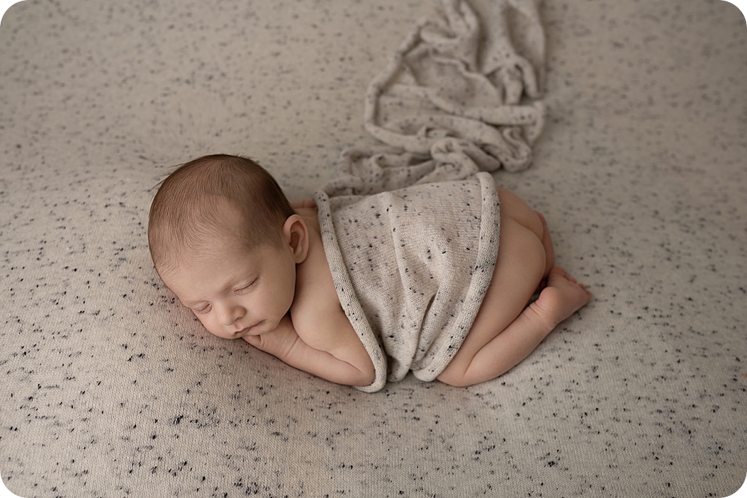 baby sleeps in speckled wrap during neutral toned newborn session