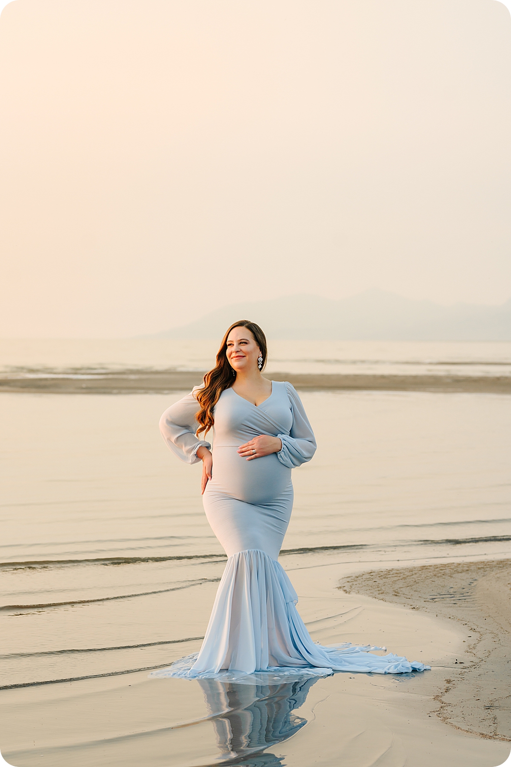 mom in blue dress holds baby belly during sunset maternity portraits on the lake