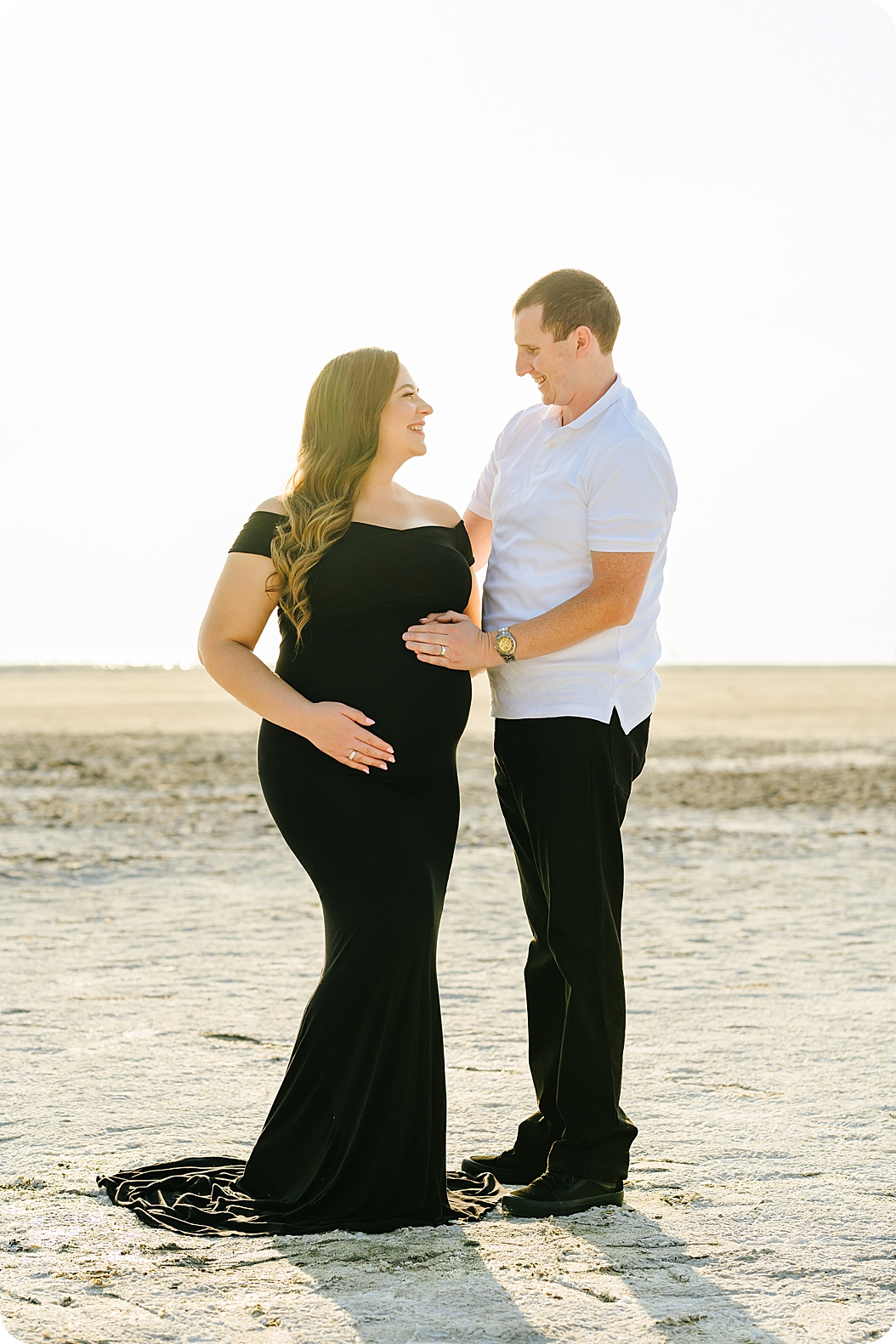 expecting parents stand in lake bed holding mom's belly