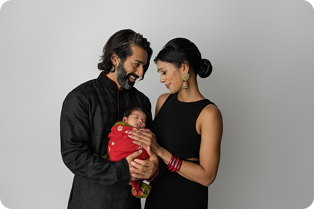 Indian parents look down at baby girl during newborn portrait in UT studio