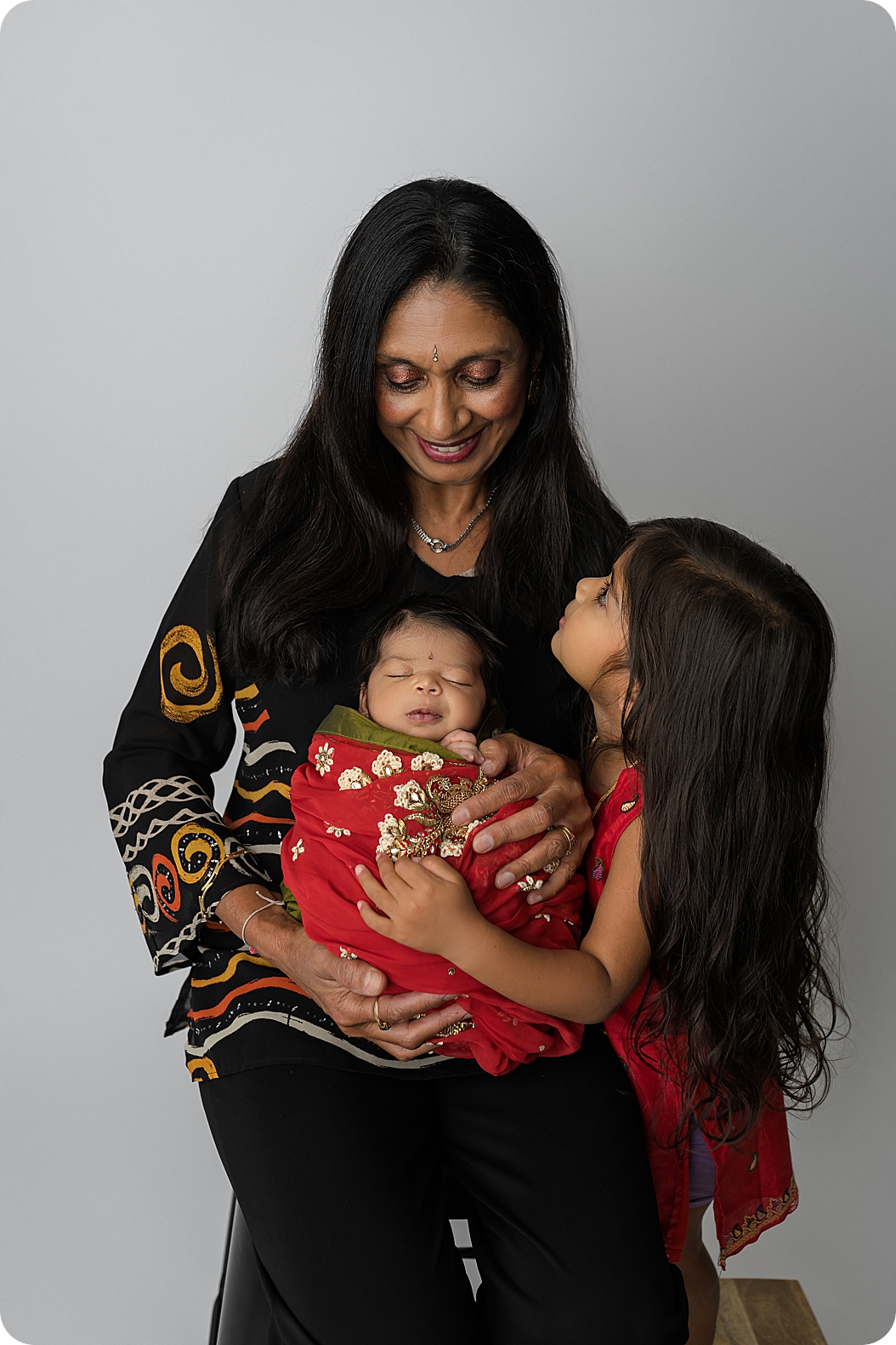 grandmother hugs newborn granddaughter and toddler during Indian Inspired Newborn Portraits 
