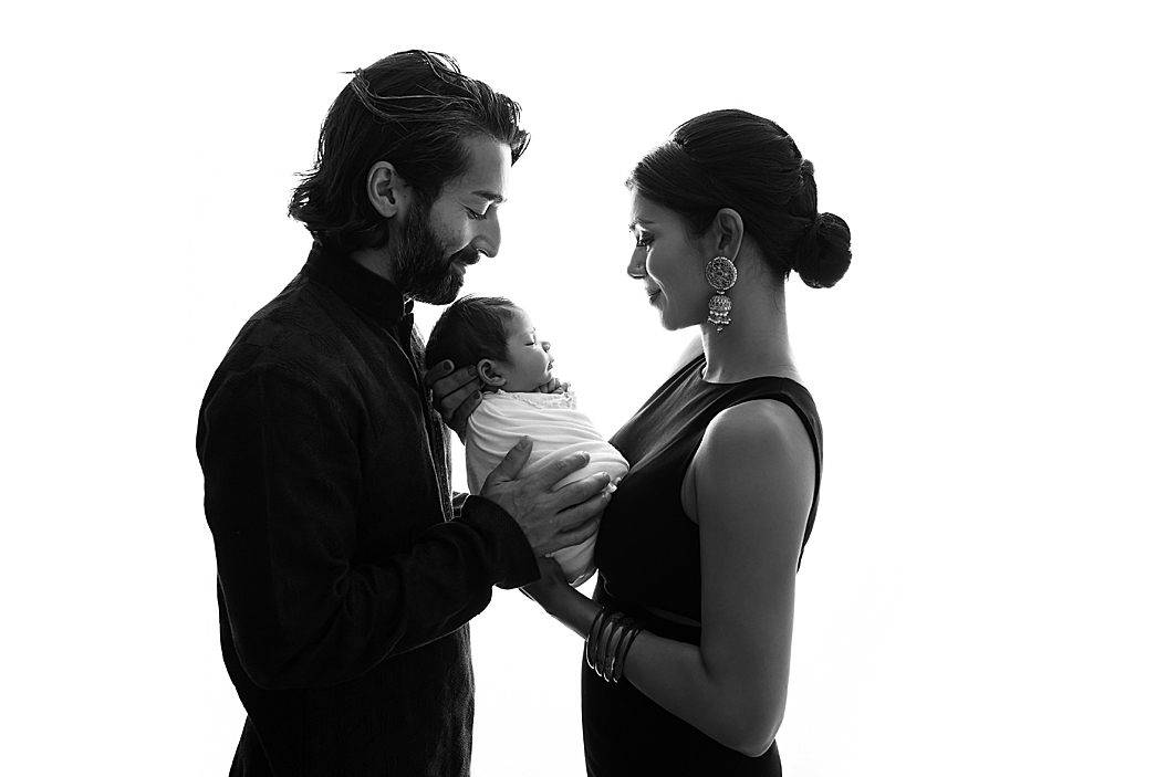 parents hold baby girl between them on white backdrop 