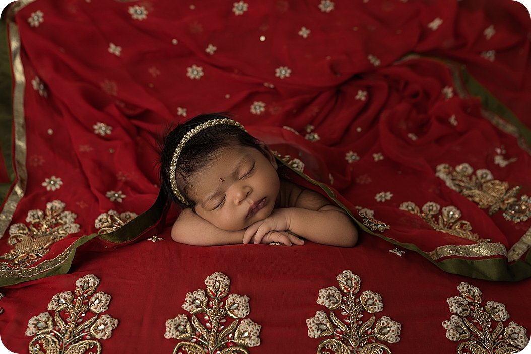 baby girl sleeps under mom's gold and red sari during Indian Inspired Newborn Portraits 