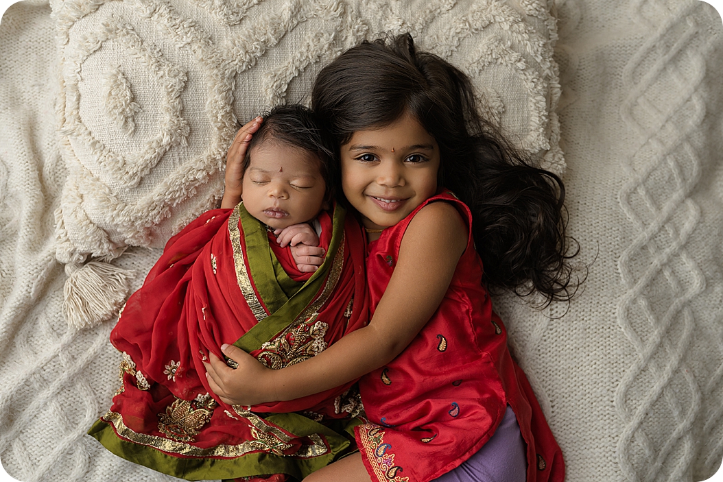 sister hugs baby girl during Indian Inspired Newborn Portraits 