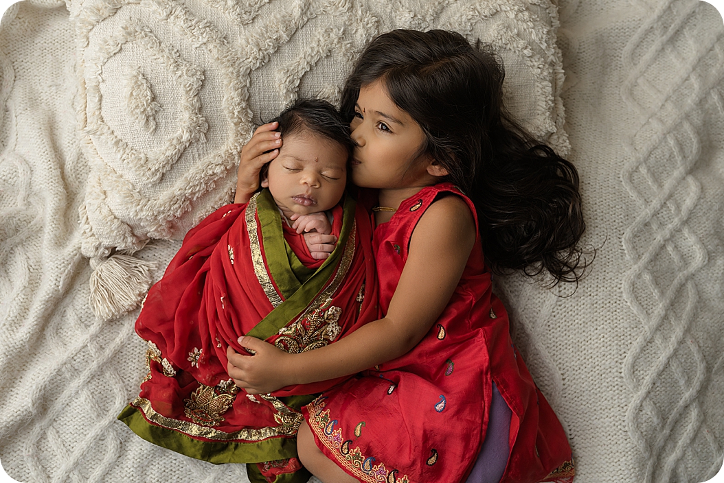 big sister kisses newborn girl during Indian Inspired Newborn Portraits 