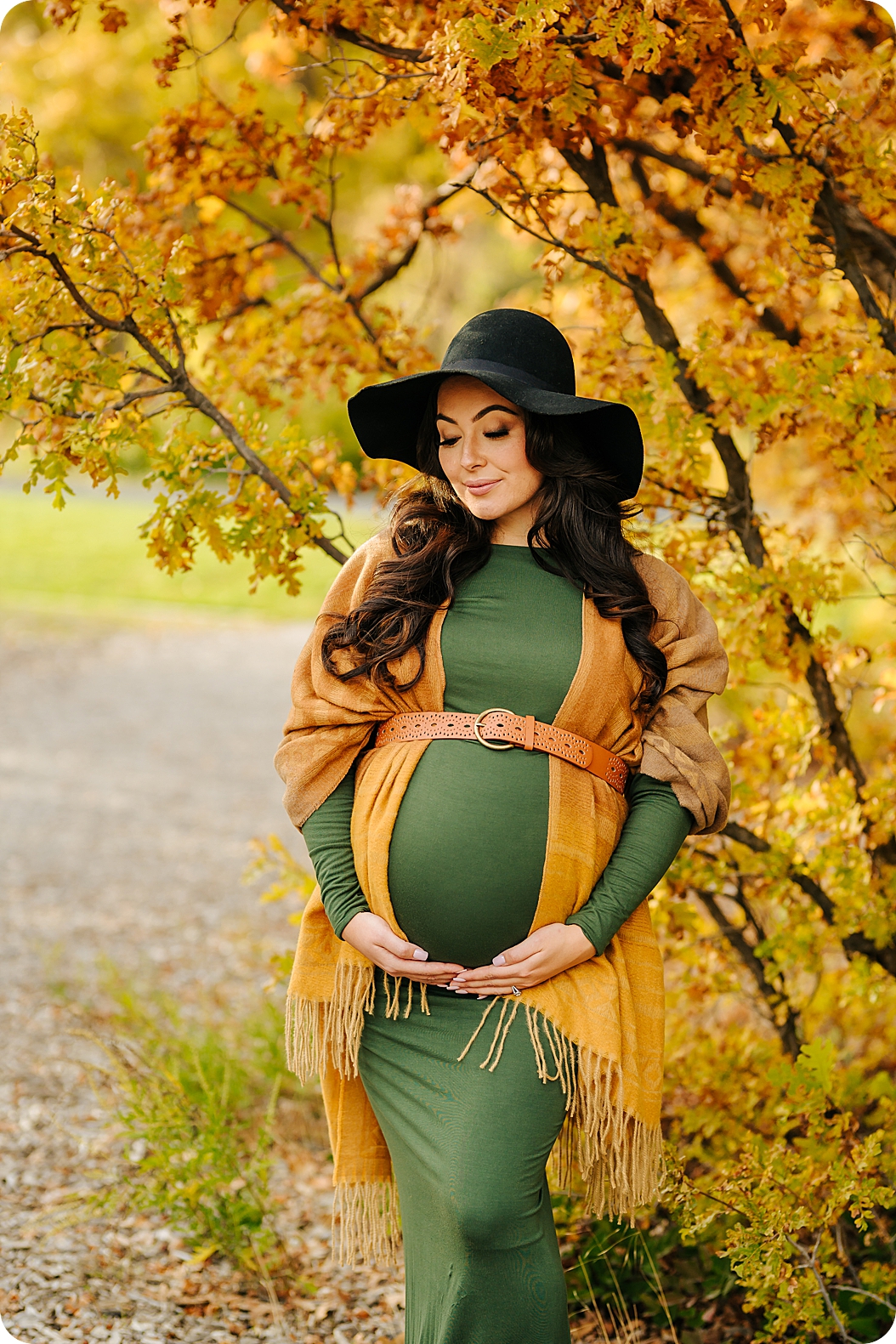 expecting mother looks down at belly during fall maternity portraits