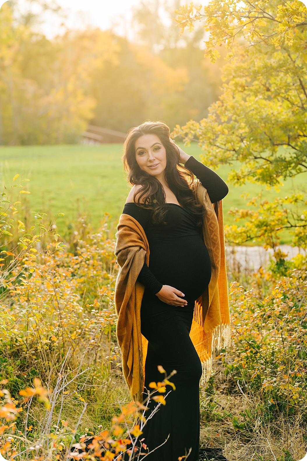 mom pushes hair back while holding belly in black dress during fall maternity session
