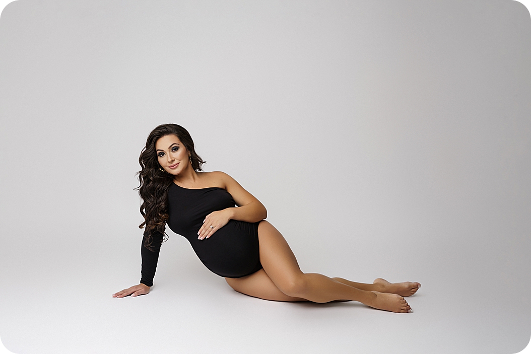 mother in black unitard lays on floor during maternity session 