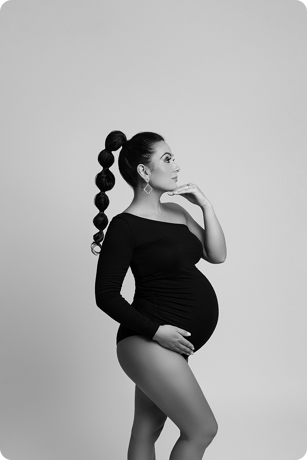 expecting mom holds belly and hand under chin during dramatic studio maternity portraits