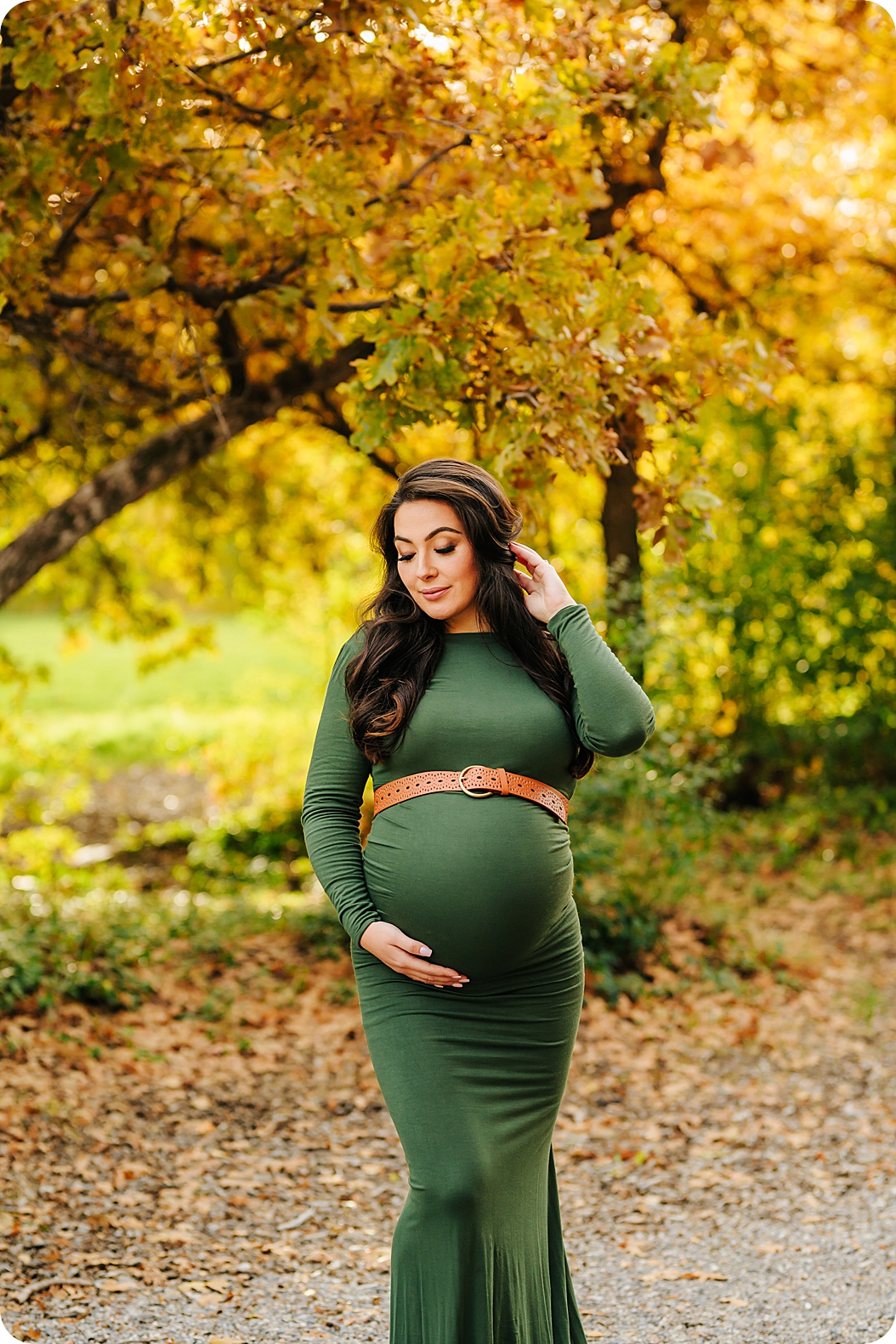 woman holds hair while holding baby belly in dark green dress