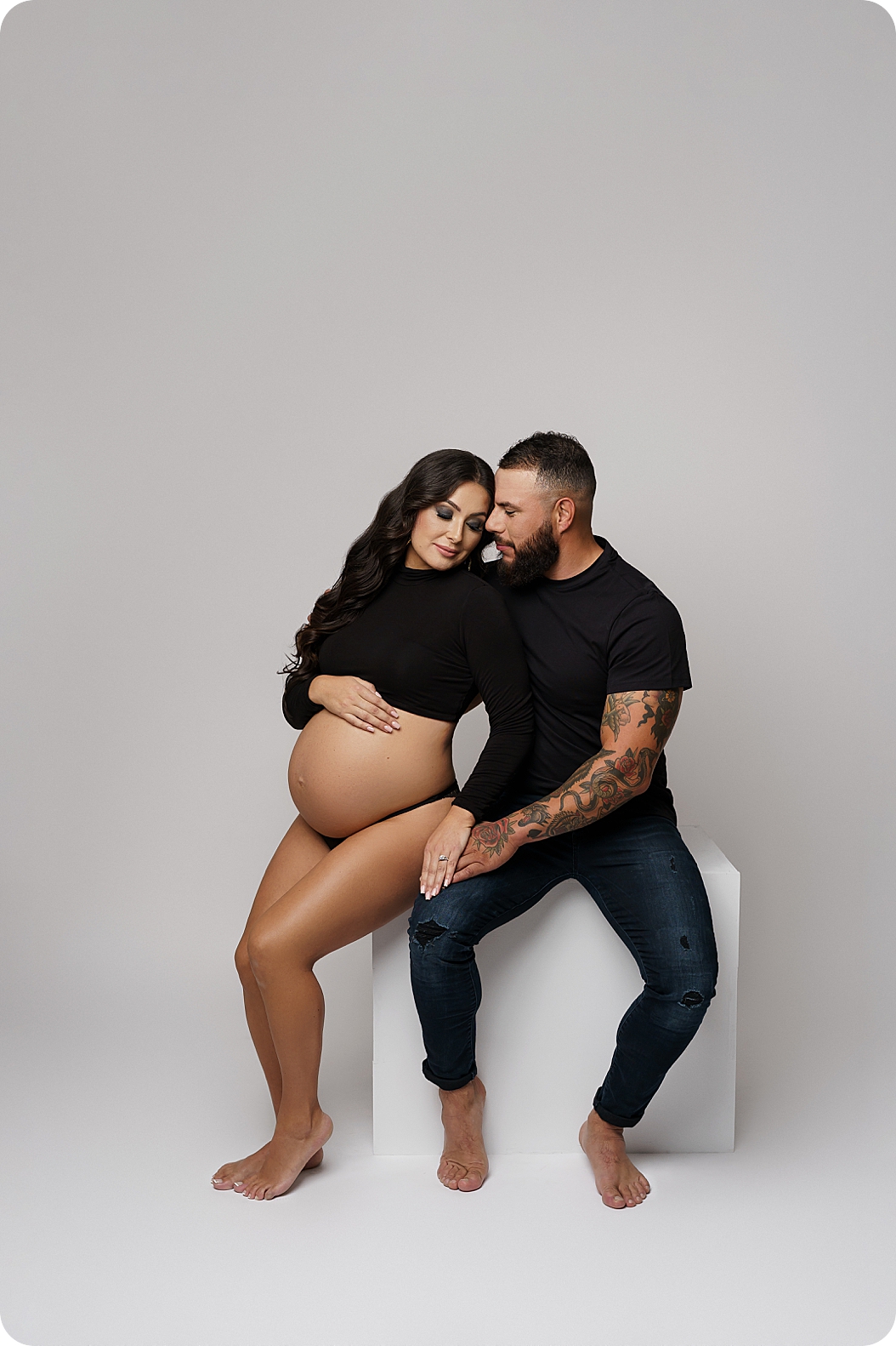 couple sits together during studio maternity photos 